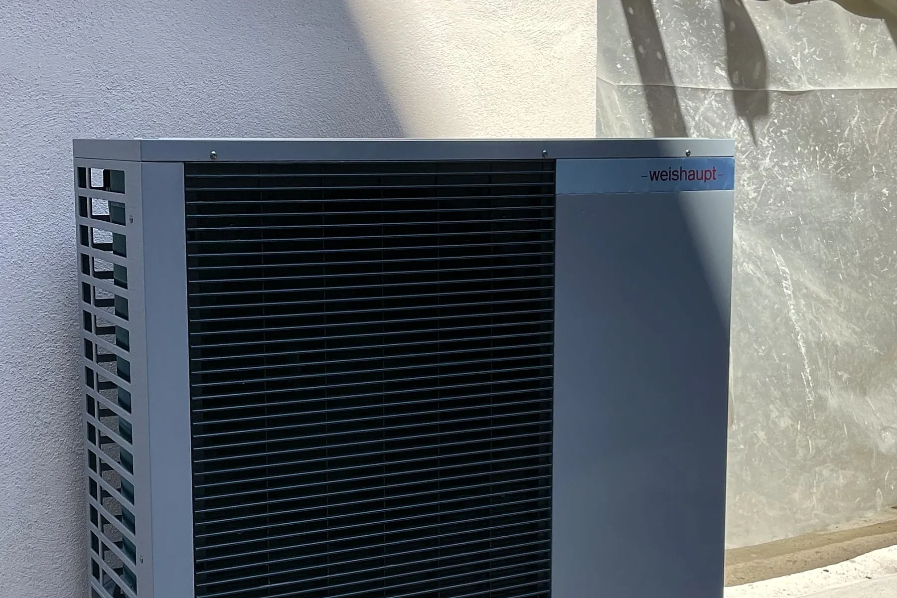 Pompa di calore monoblocco grigio antracite installata all'esterno, contro un muro intonacato