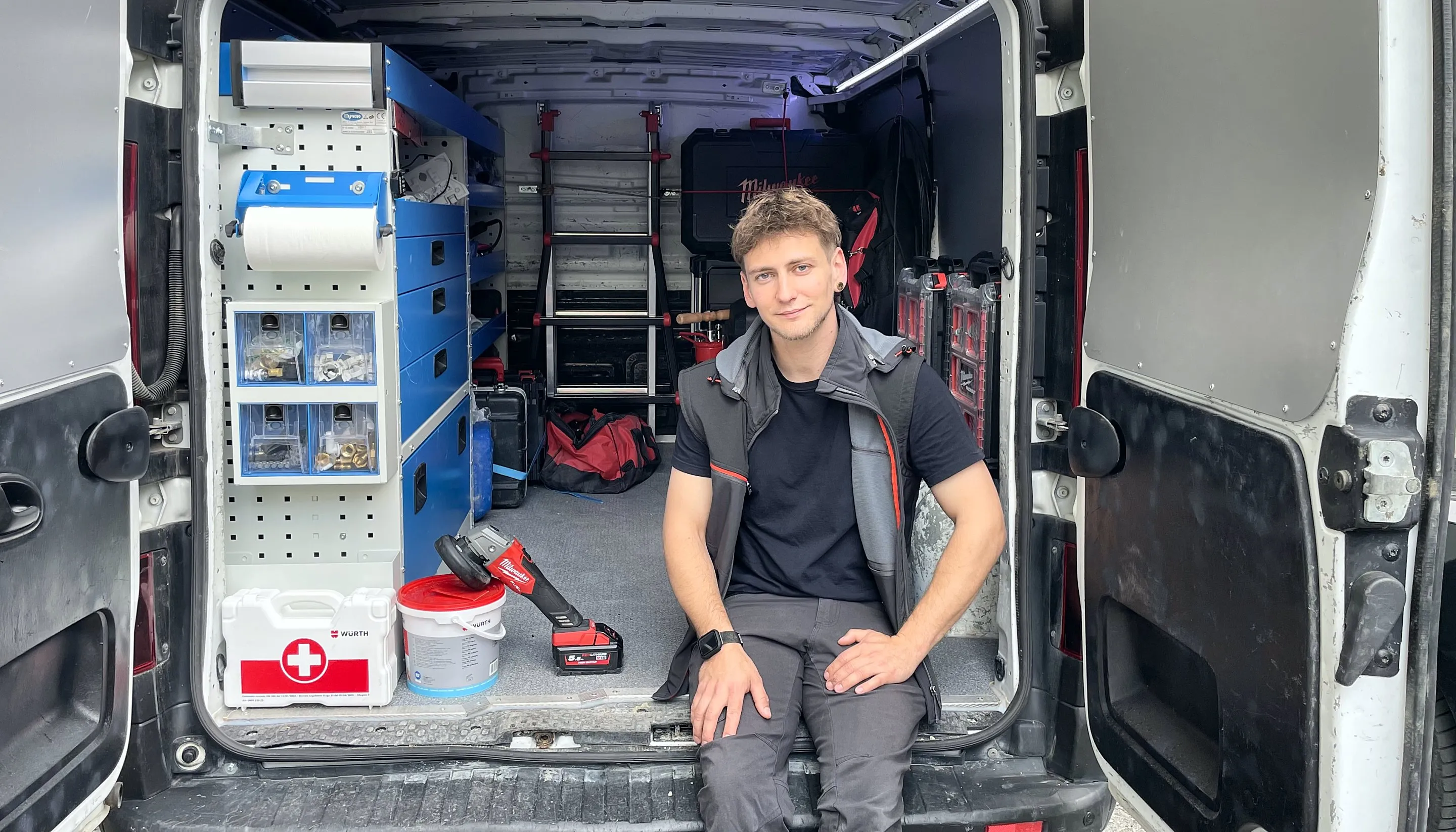 Alessio Aldrighetti seduto sul retro del furgone aperto, con gli scaffali in ordine, le cassette dei raccordi e gli attrezzi