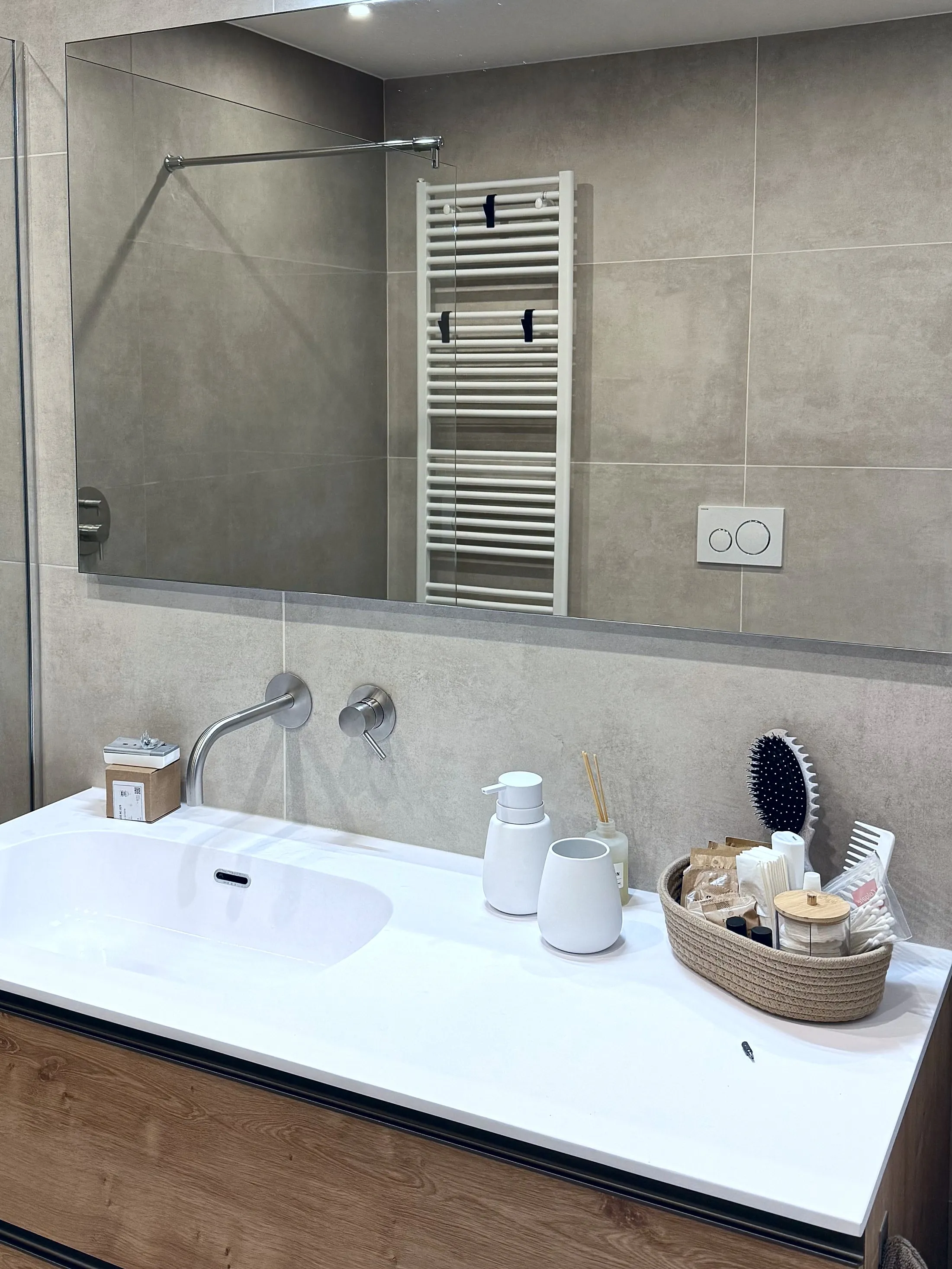 Bagno ristrutturato: mobile sospeso in legno con il piano lavabo bianco, rubinetto a parete e specchio grande con la luce sopra