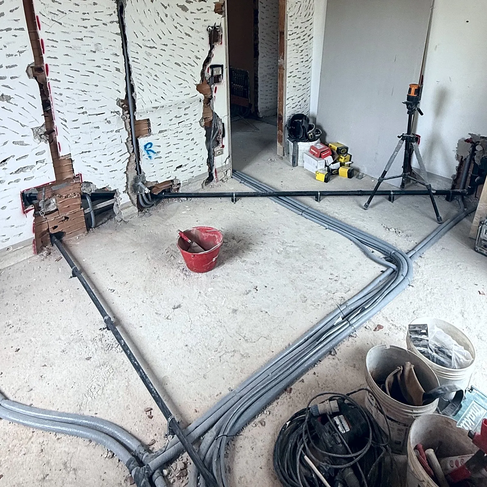 Appartamento a muri aperti: le linee dell'impianto posate a pavimento, con le curve allineate, e la livella laser sul treppiede