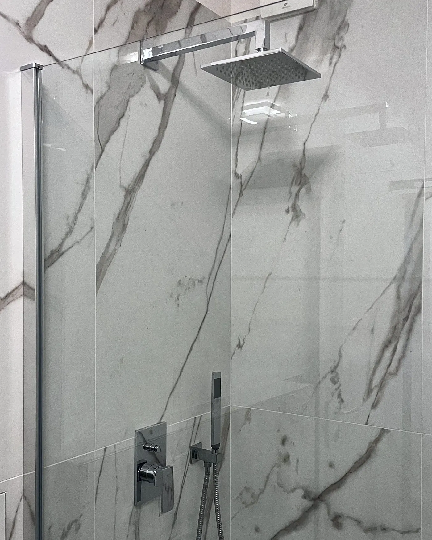 Doccia appena finita con parete in vetro, rivestimento in gres effetto marmo, soffione a pioggia e miscelatore a incasso