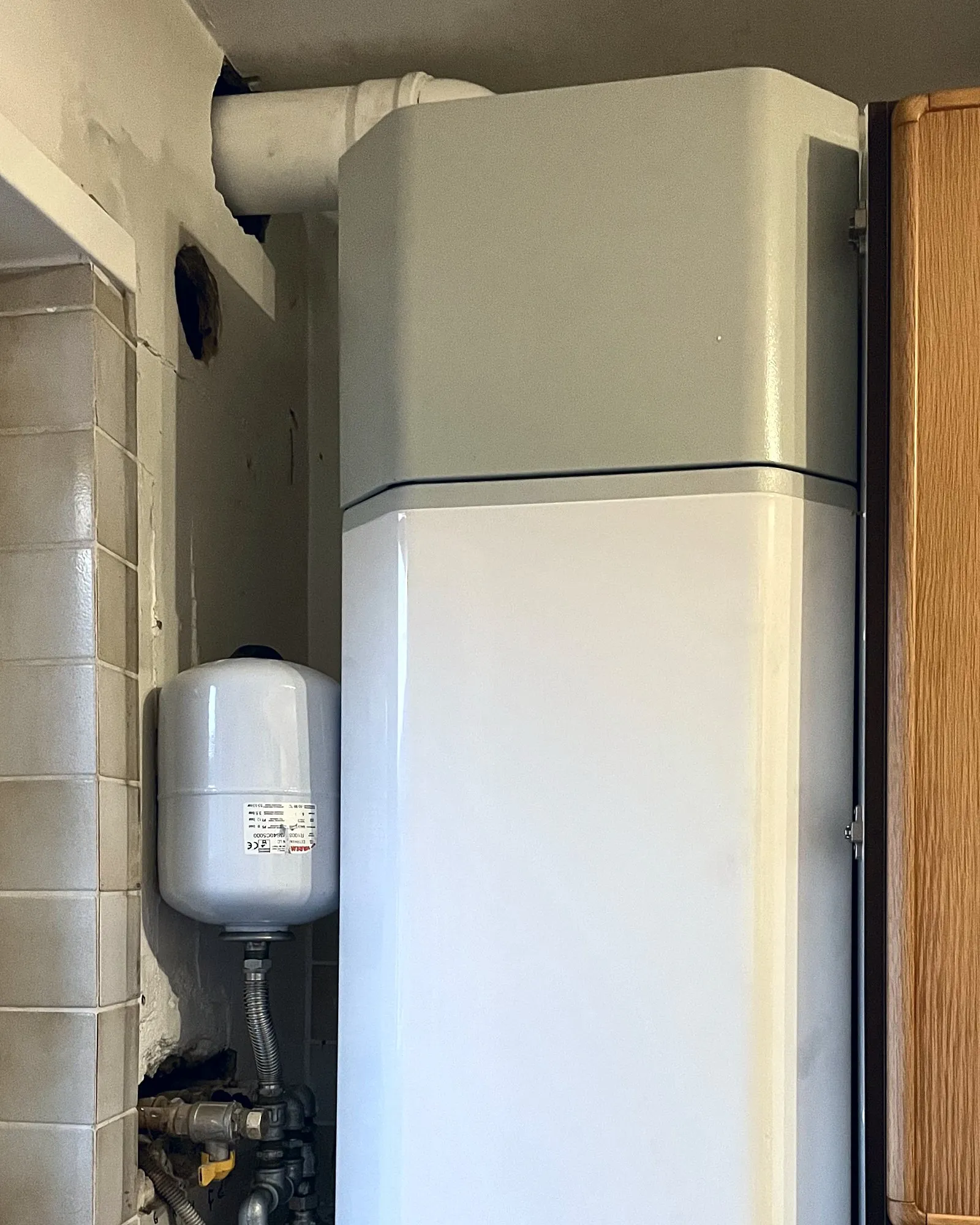 Scaldabagno a pompa di calore bianco installato in una nicchia, con il vaso di espansione e i raccordi accanto